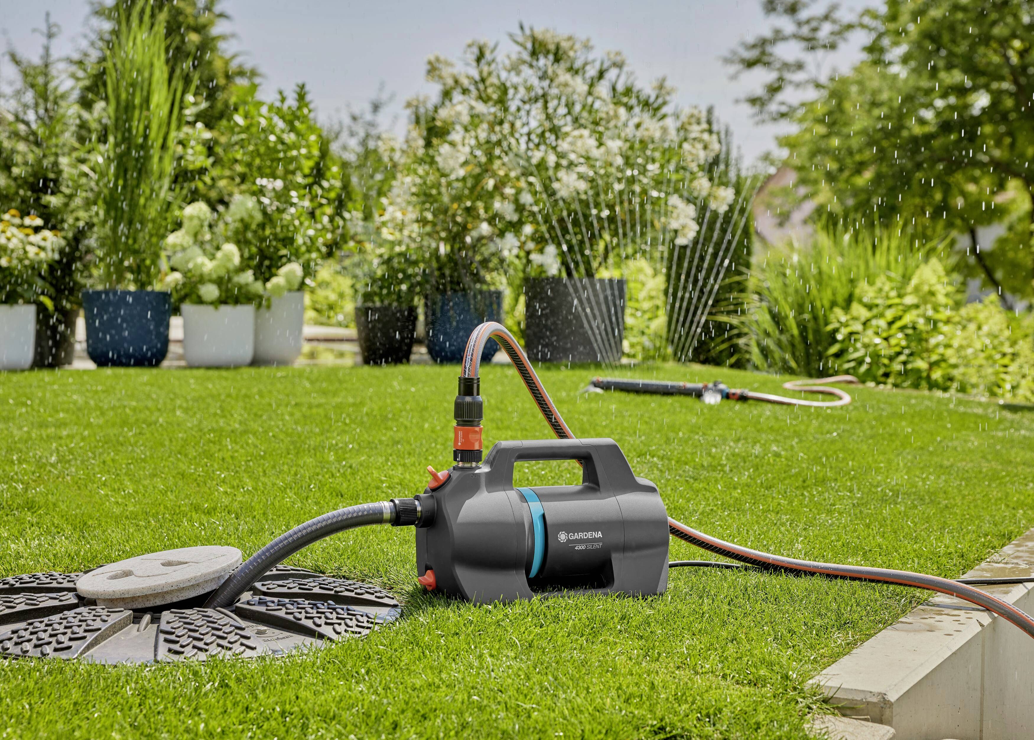 Ein elektrischer Gartenbewässerungspumpe steht auf einem grünen Rasen, verbunden mit einem Wasserschlauch, um Pflanzen zu bewässern.