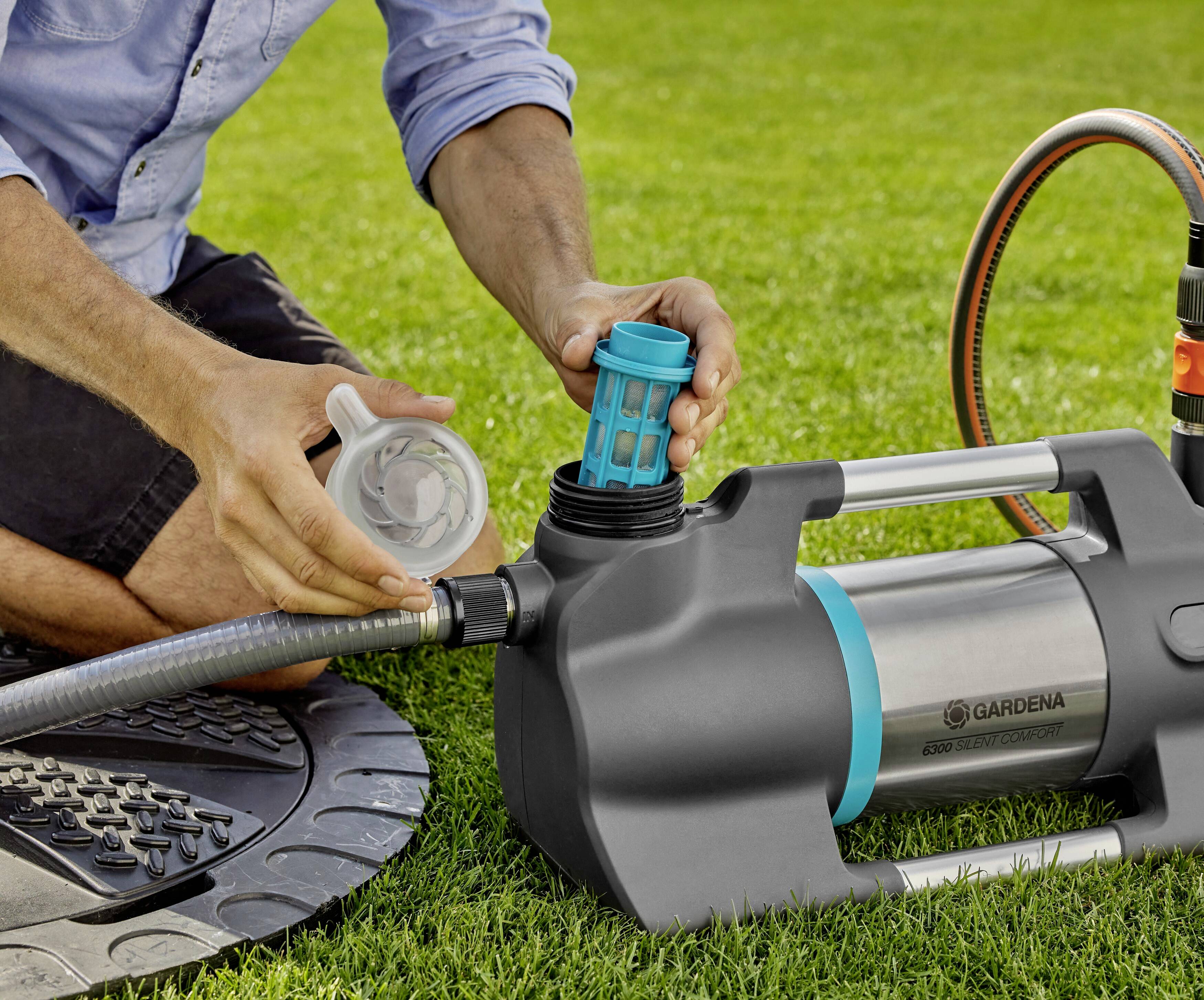 Eine Person reinigt den Filter einer Gartenpumpe auf einer Rasenfläche. Die Pumpe ist an einen Wasserschlauch angeschlossen.