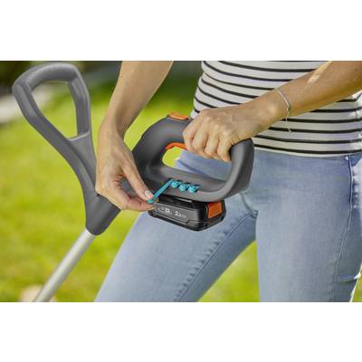 Eine Person montiert eine Batterie an einem Gartengerät im Freien. Sie trägt Jeans und ein gestreiftes Shirt.
