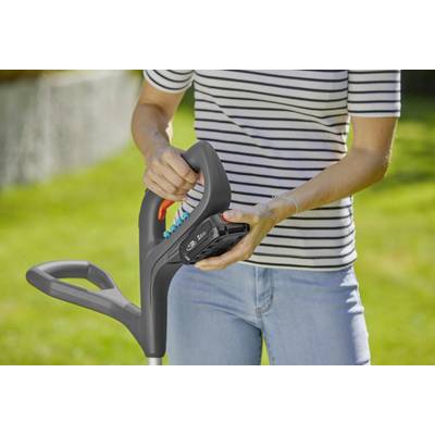 Eine Person hält einen Rasenmähergriff in einem Garten. Der Fokus liegt auf der Handhabung des Geräts.
