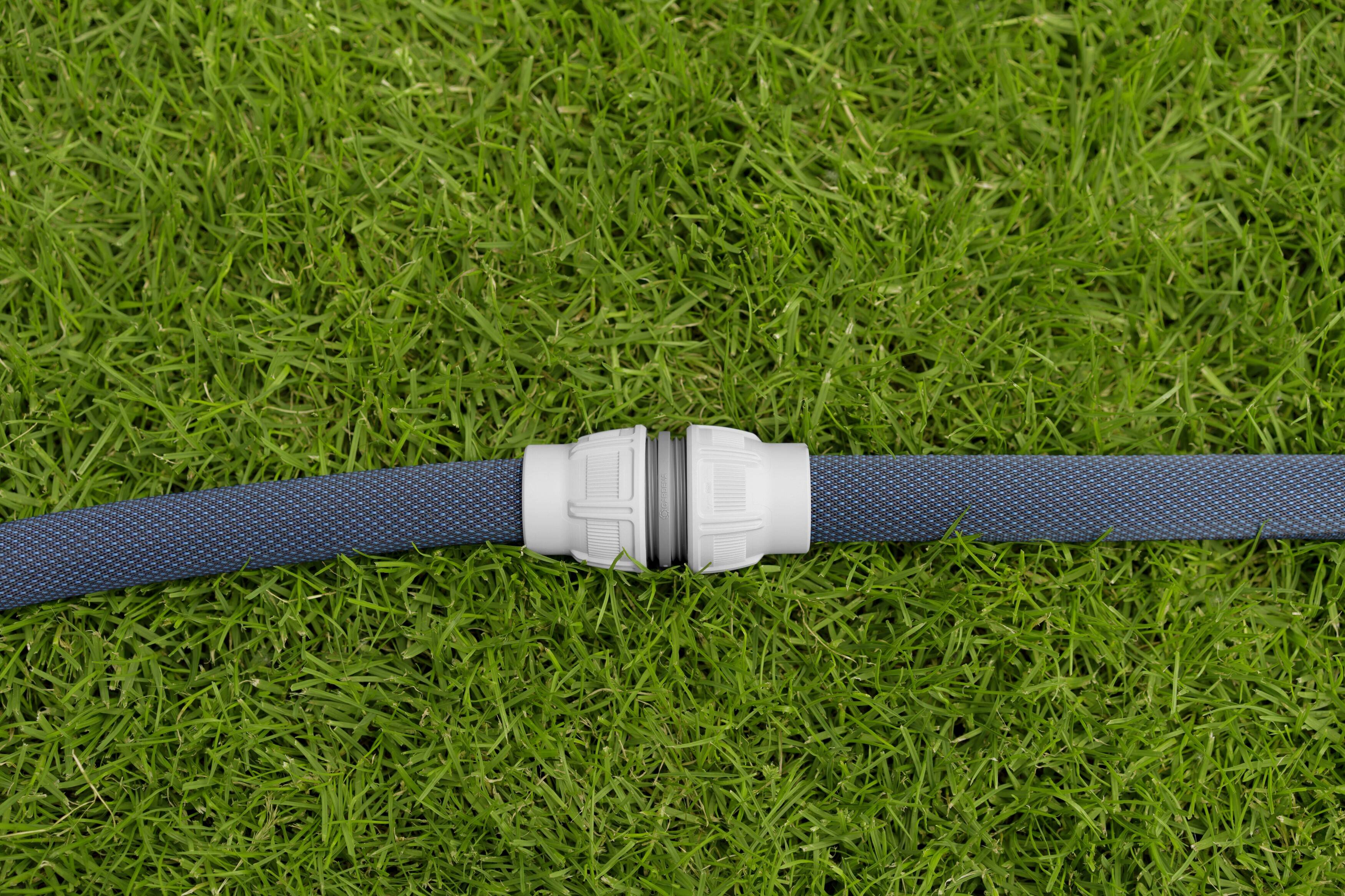 Ein blauer Gartenschlauch liegt mit einer weißen Kupplung verbunden auf grünem Gras.