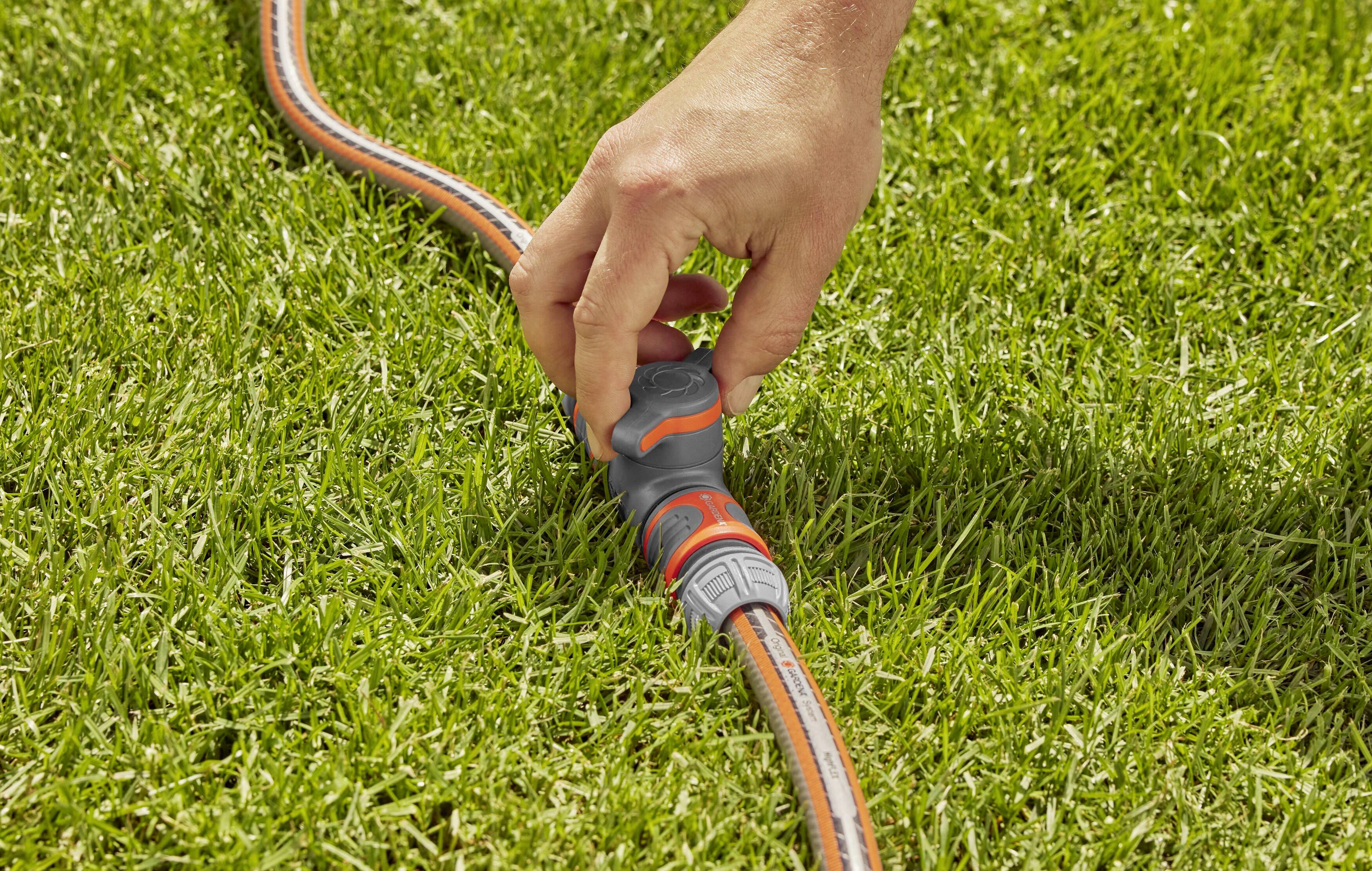 Eine Hand dreht einen Gartenschlauchadapter auf einem grünen Rasen, um Wasserfluss zu regulieren.
