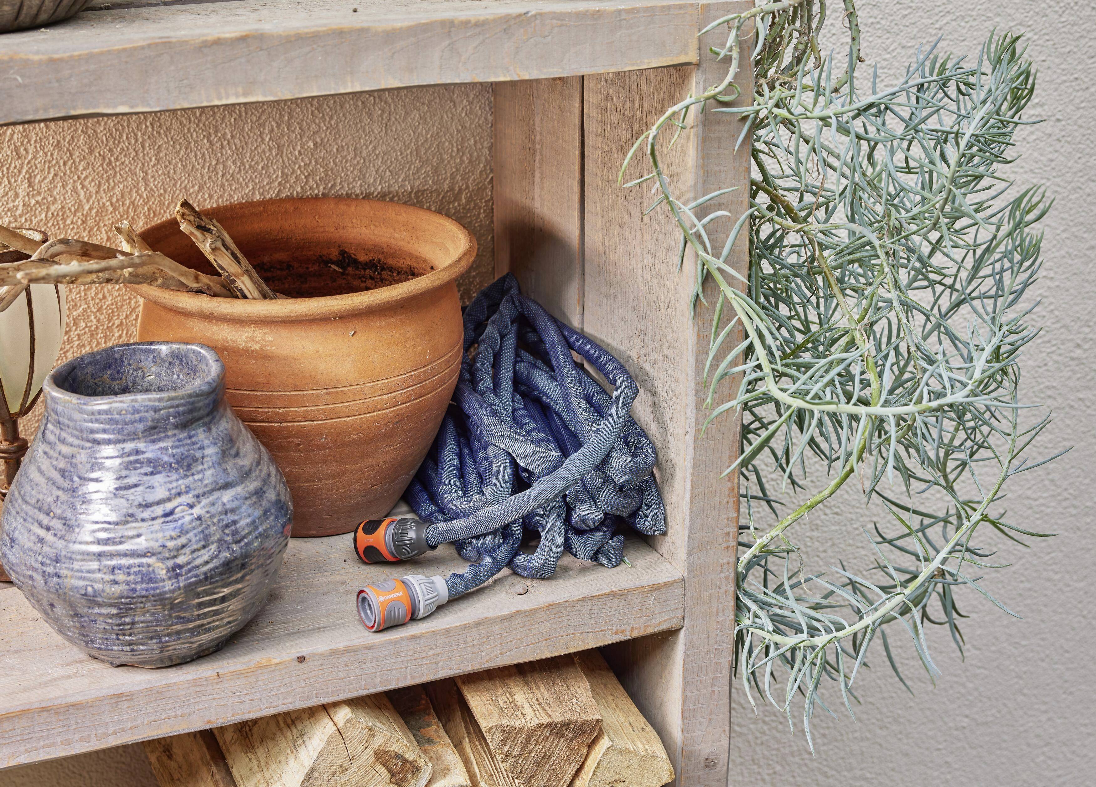 Ein Holzregal mit Tontöpfen, einer blauen Vase, einem zusammengerollten Gartenschlauch und einer hängenden Pflanze.