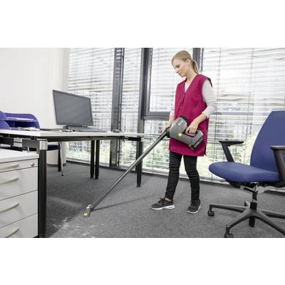 Eine Person in einer rosa Weste saugt einen Teppichboden in einem Büro in der Nähe eines Schreibtisches mit einem Computermonitor, Aktenschränken und einem Bürostuhl.