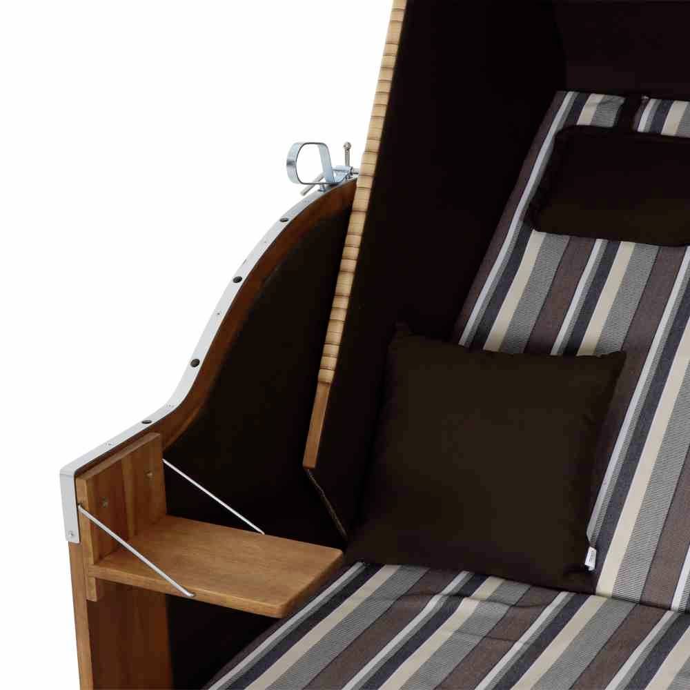 Ein Strandkorb mit gestreiftem Stoff und schwarzen Kissen, seitlich ein kleines Tischchen aus Holz.