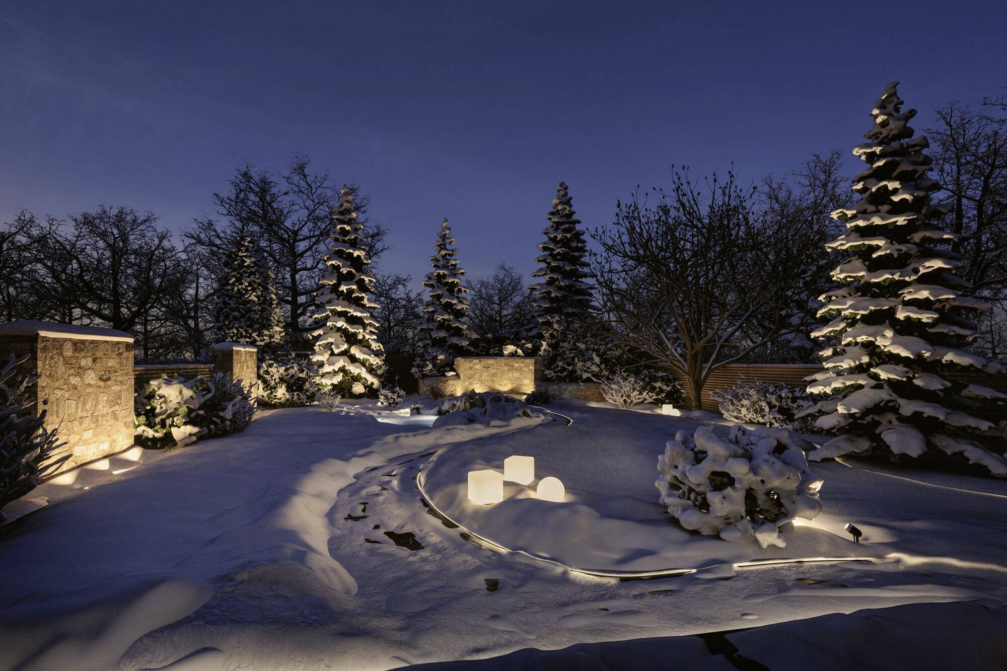 Ein verschneiter Garten bei Nacht, beleuchtet von warmen Lichtern, umgeben von schneebedeckten Bäumen und Sträuchern.