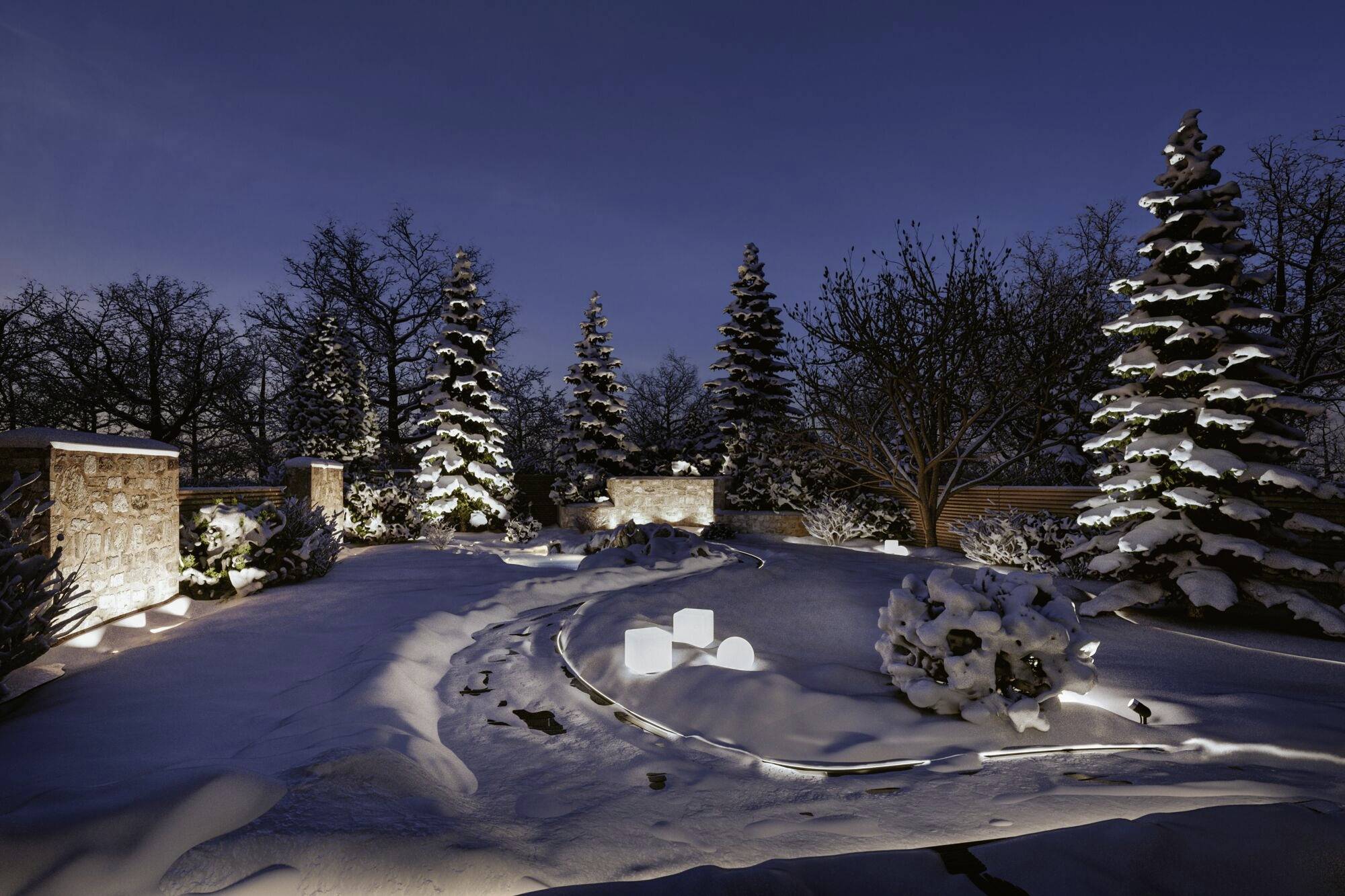 Ein verschneiter Garten bei Nacht, beleuchtet von warmem Licht. Bäume und Sträucher sind schneebedeckt, klare Himmel im Hintergrund.