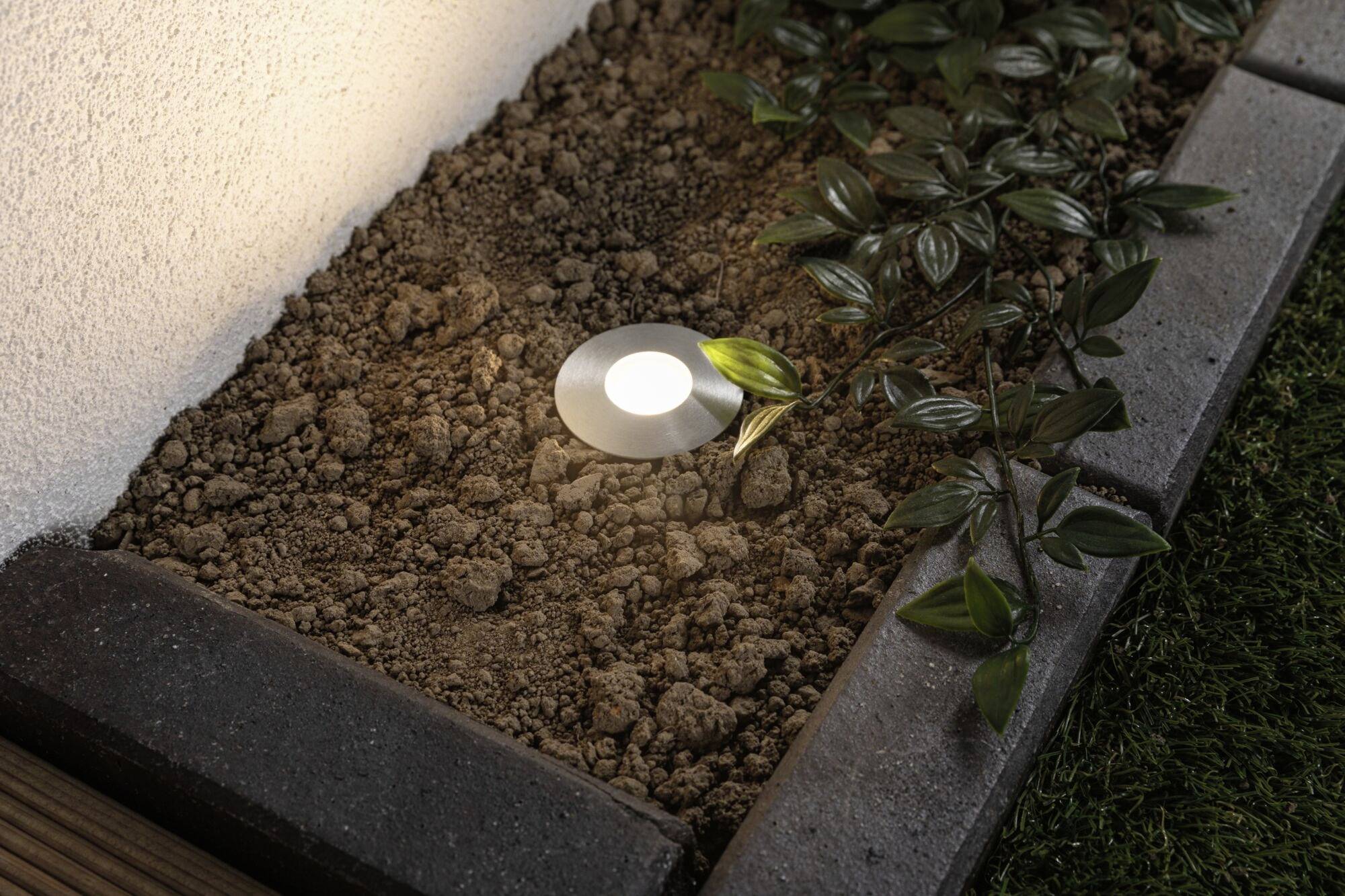 Beleuchtetes Beet: Bodenleuchte eingebettet in Erde neben Pflanzen und Gartenkantensteinen.