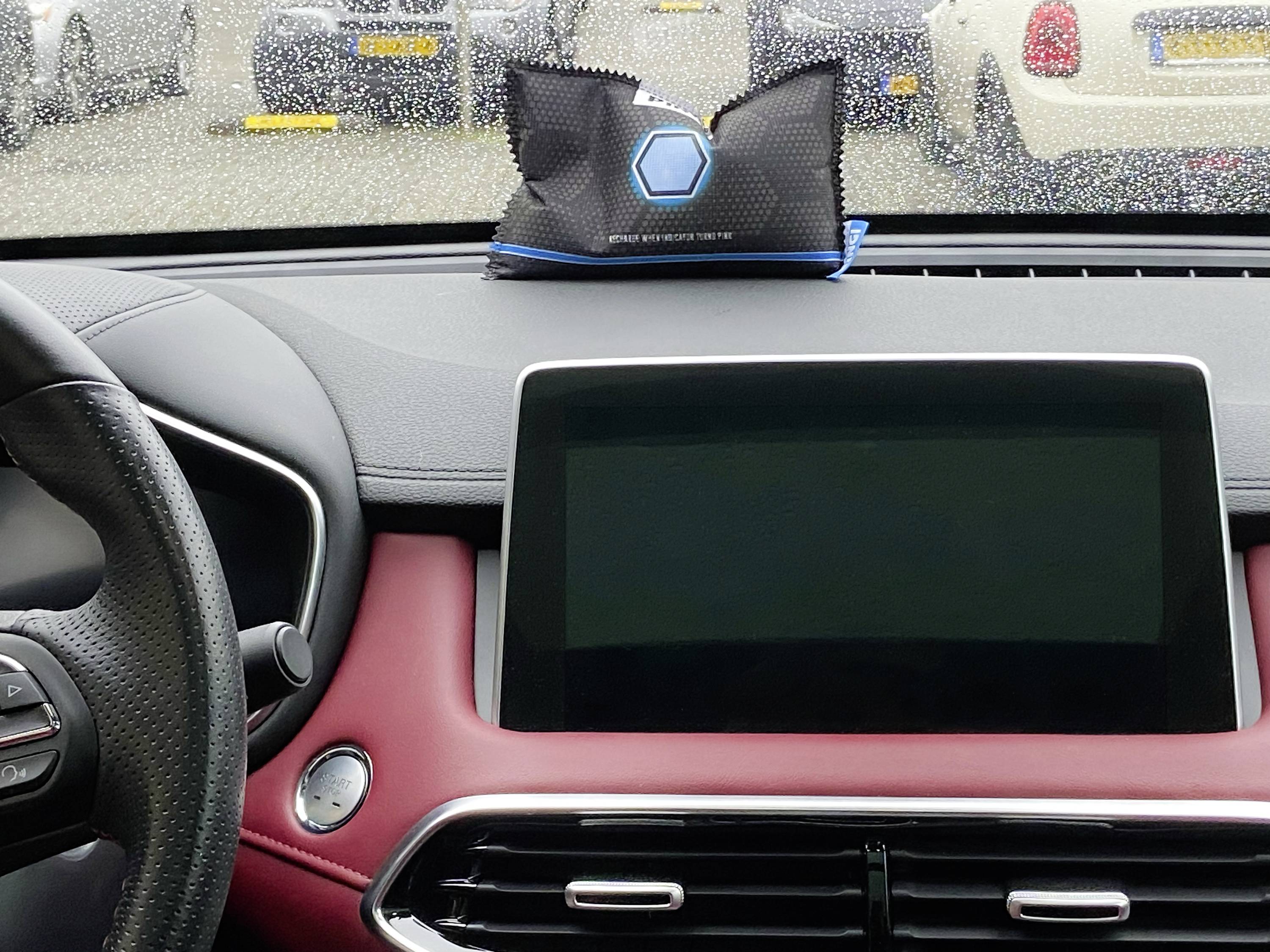 Innenraum eines Autos bei Regen. Ein digitales Display im Armaturenbrett ist ausgeschaltet. Ein Beutel liegt auf dem Armaturenbrett.