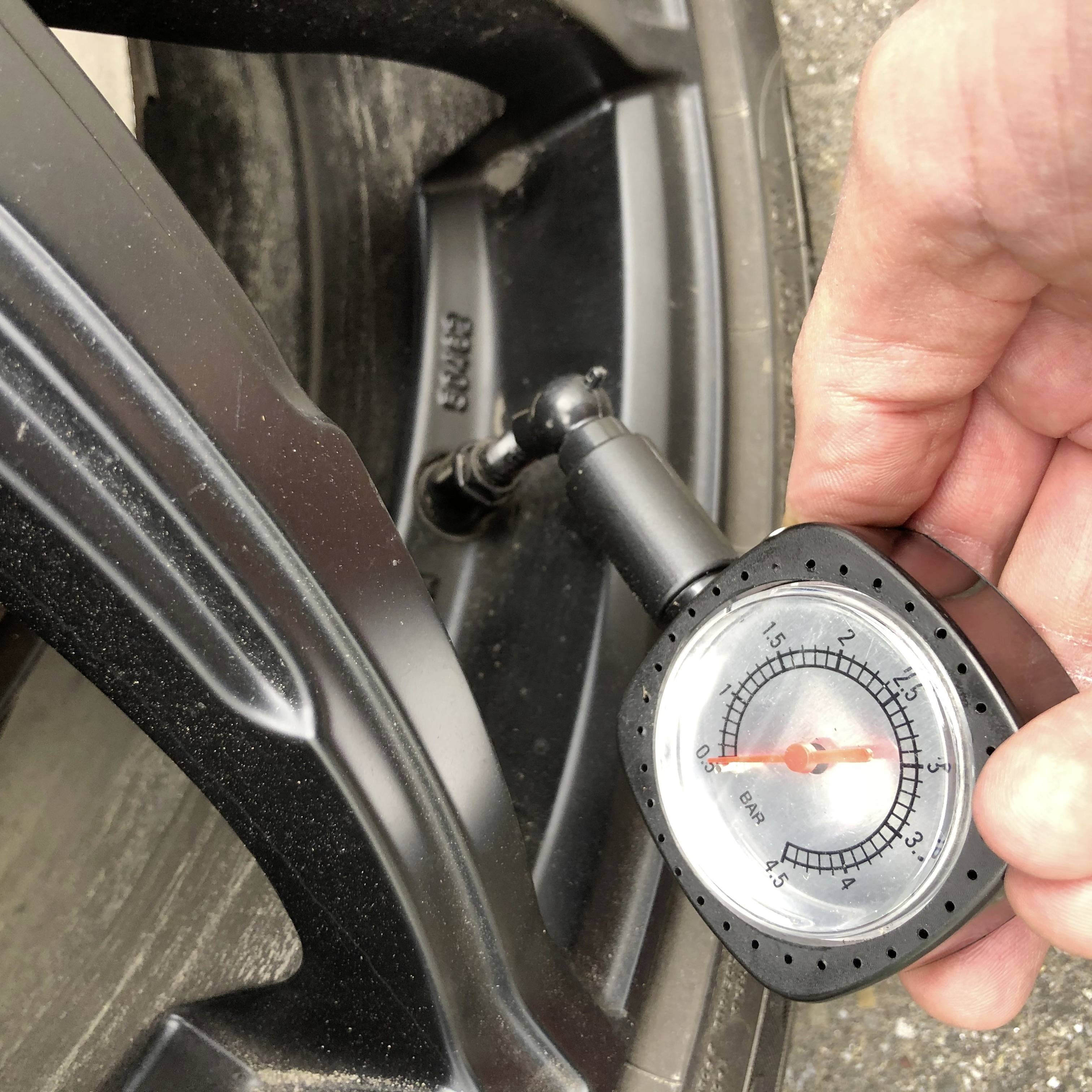 Ein Manometer zeigt 2,5 bar Reifendruck an, das Manometer wird von einer Hand gehalten und ist an einem Autoreifenventil angebracht.