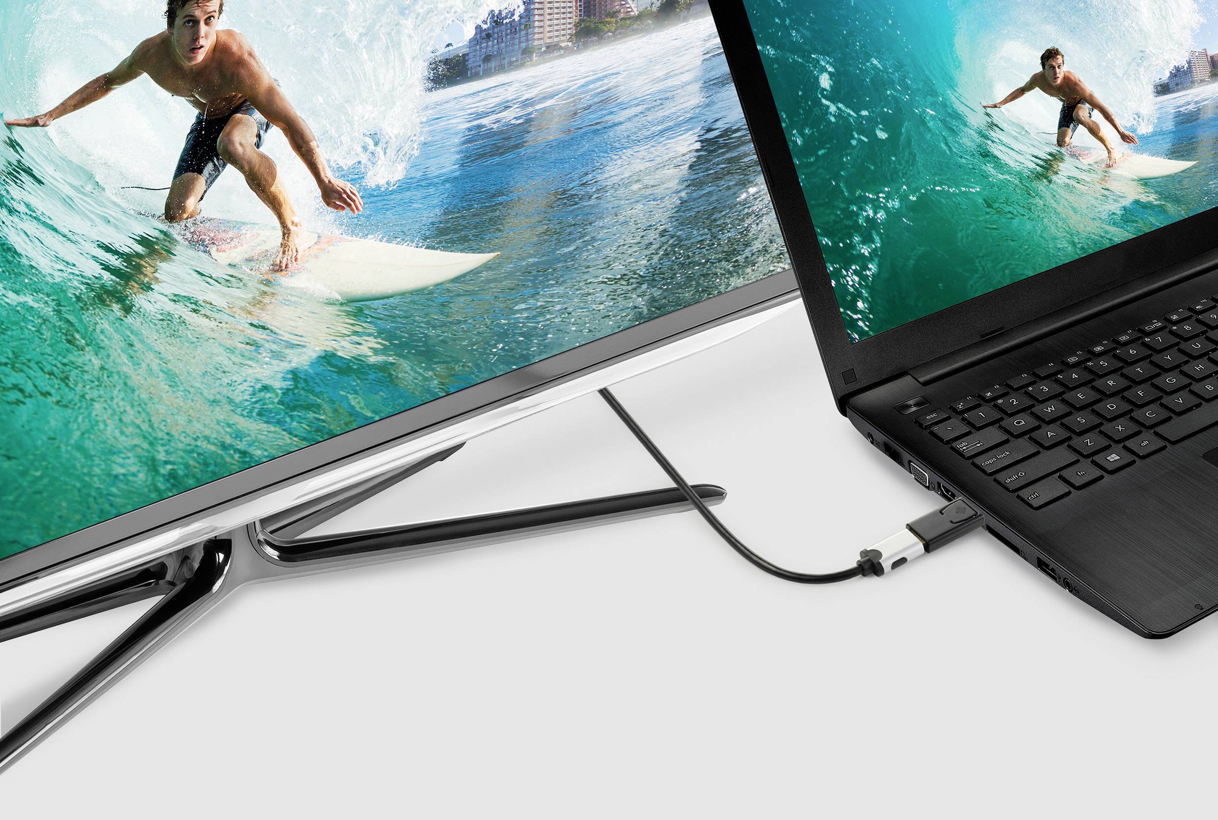 Ein Laptop ist über ein Kabel mit einem größeren Monitor verbunden. Der Monitor zeigt ein Bild von einem Surfer auf einer Welle.