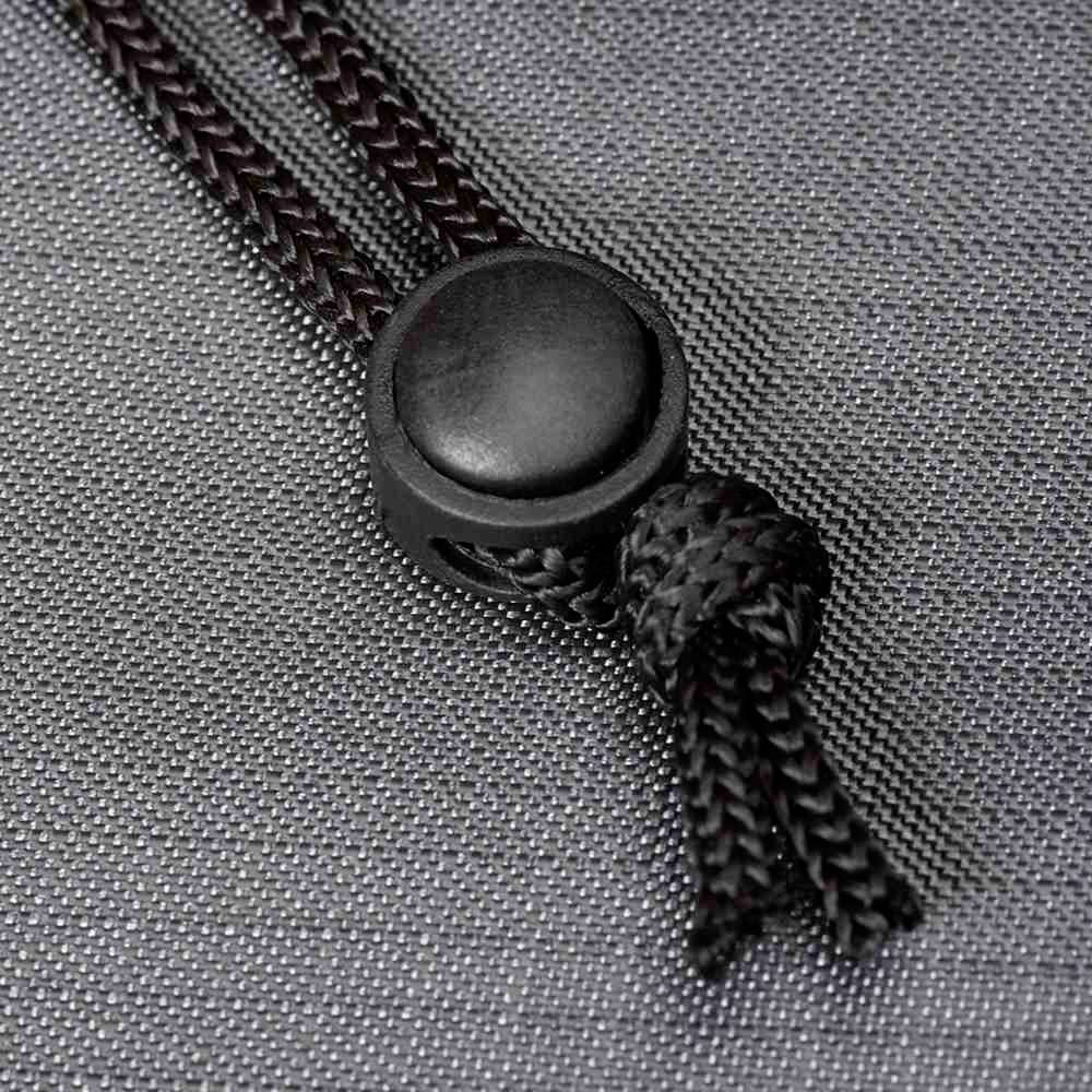 Schwarze Kordel mit Knoten und Kunststoffknopf auf grauem Textilhintergrund. Fokus auf Details der Verschlussmechanik.
