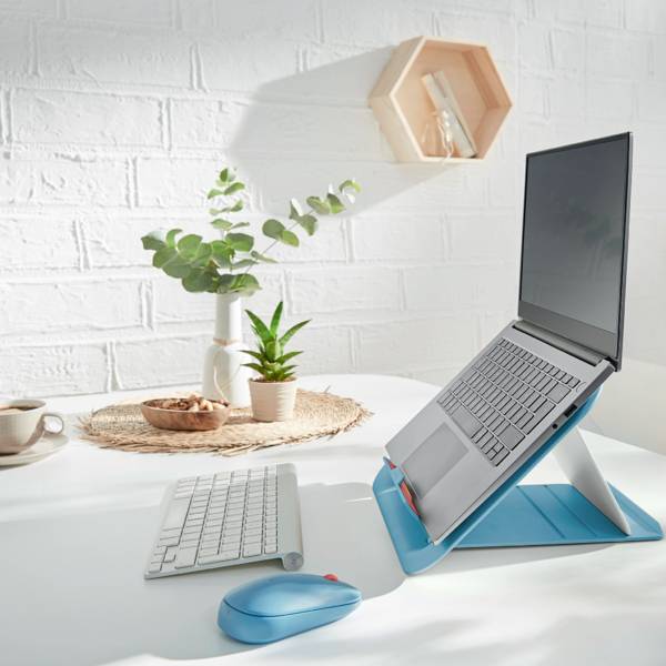 Ein Laptop steht aufrecht auf einem Ständer auf einem weißen Schreibtisch. Nebendran sind eine Pflanze, eine Tasse und eine Tastatur.