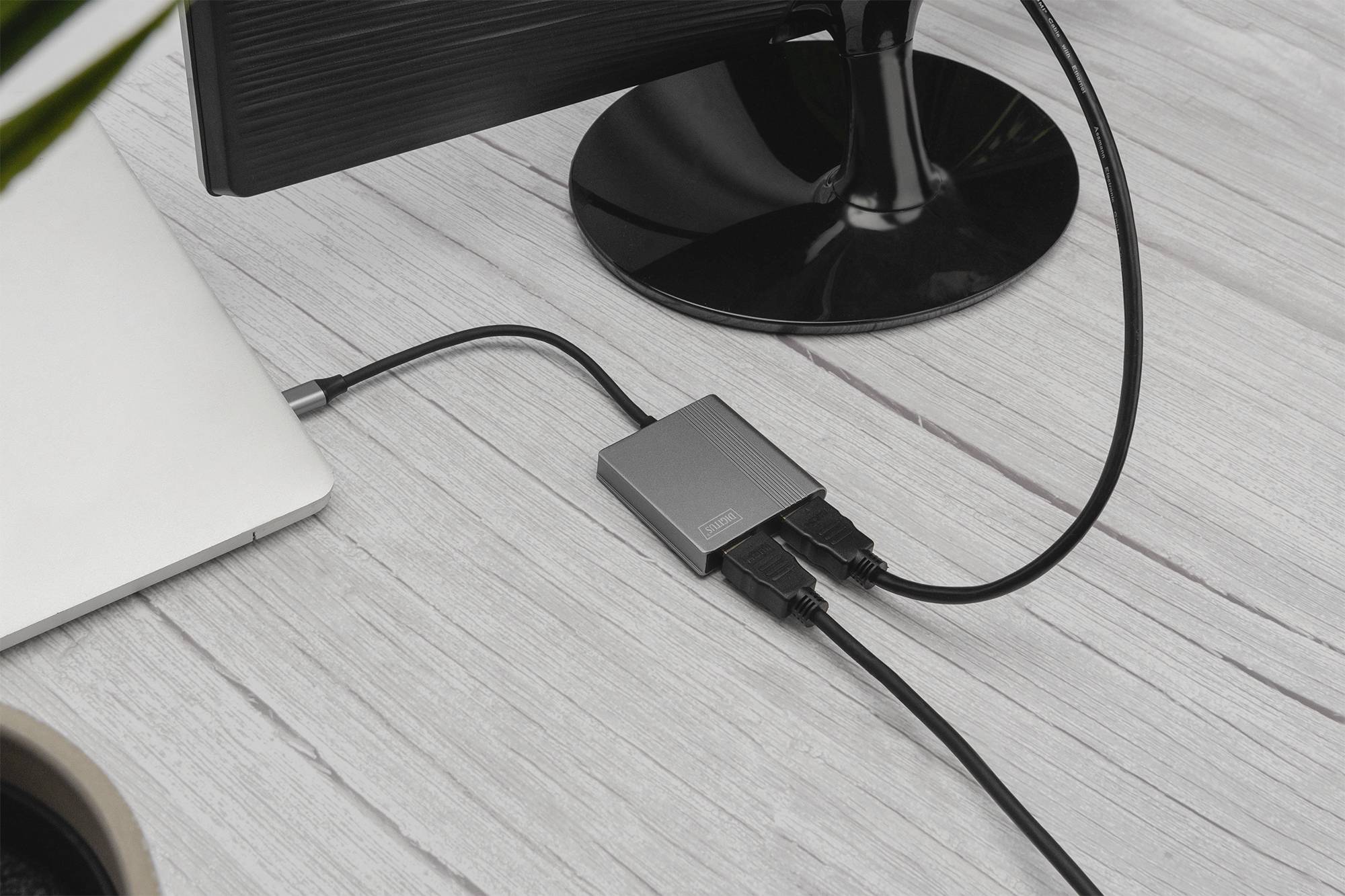 Externer Adapter verbindet Laptop mit Monitor auf einem Schreibtisch. Kabel und Anschlüsse sichtbar. Technologie und Vernetzung.