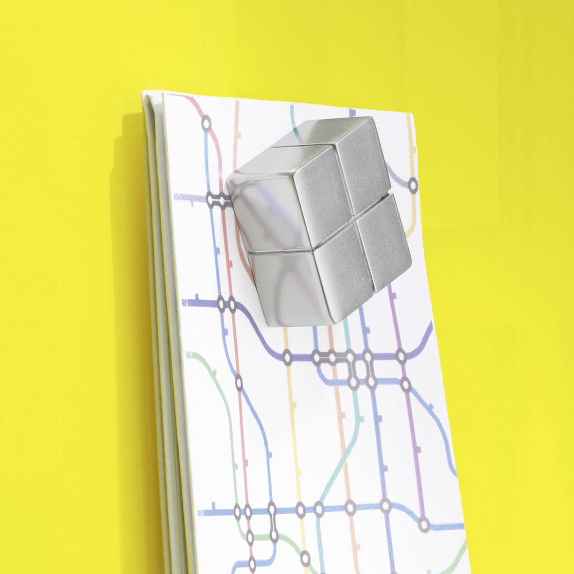 Ein silberner Würfel schwebt leicht über einem illustrierten U-Bahn-Plan auf gelbem Hintergrund.