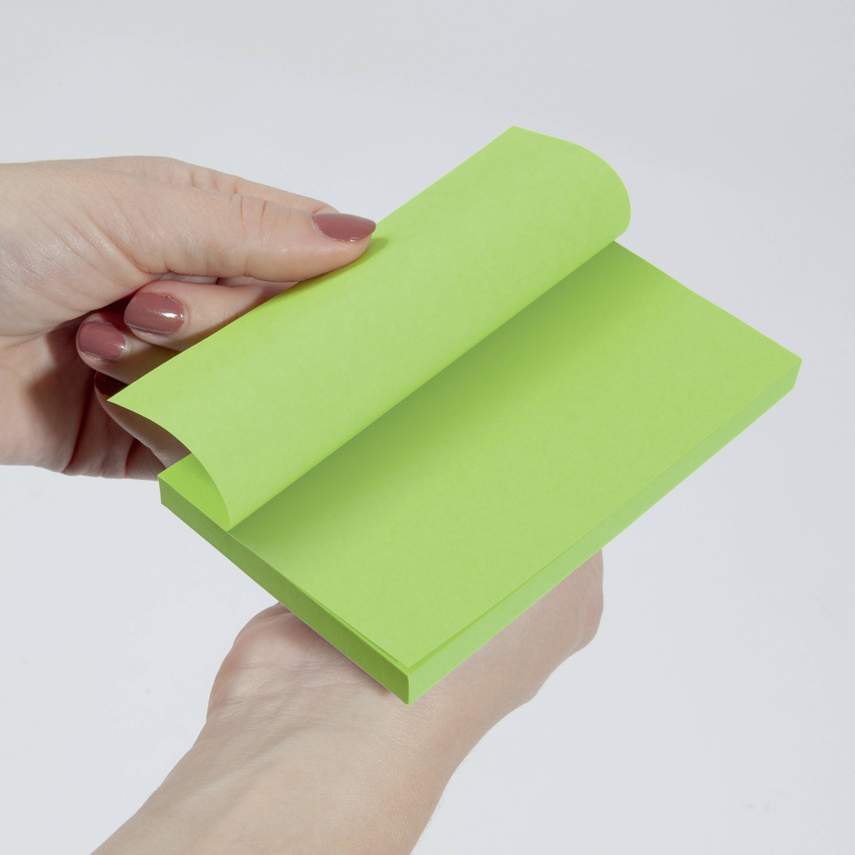 Zwei Hände halten einen grünen Notizblock, der an einer Seite aufgeschlagen ist, vor einem grauen Hintergrund.