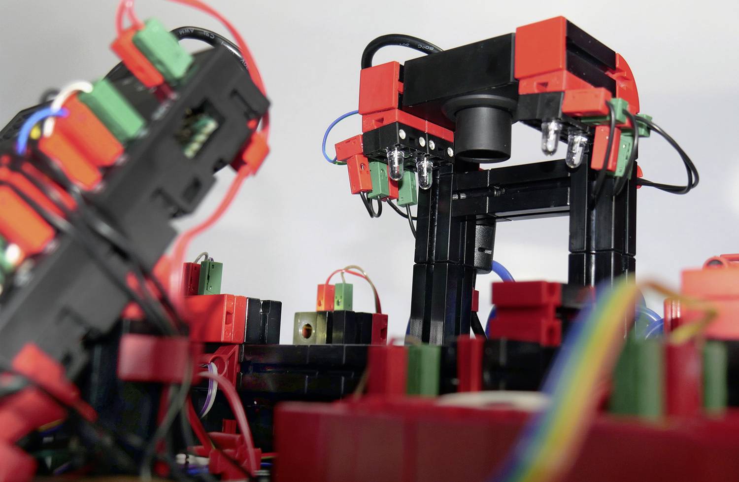 Ein Roboterarm aus roten und schwarzen Bauteilen mit Kabelverbindungen arbeitet in einer industriellen Umgebung.