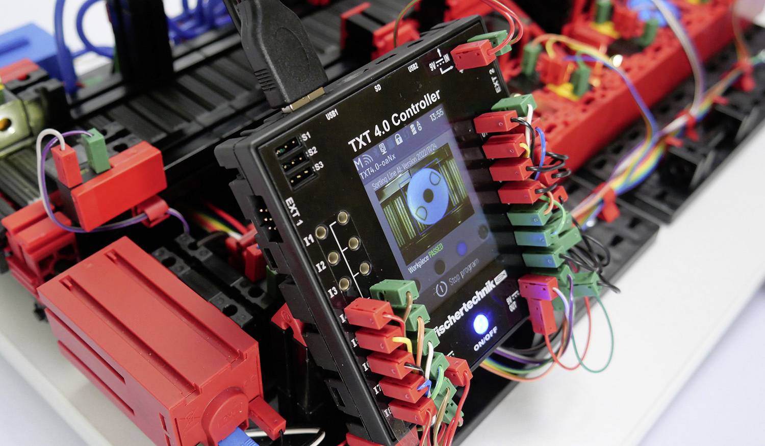 Ein Controller mit Bildschirm zeigt ein digitales Display an. Umgeben von bunten Kabeln und roten Steckverbindungen auf einer Konstruktion.