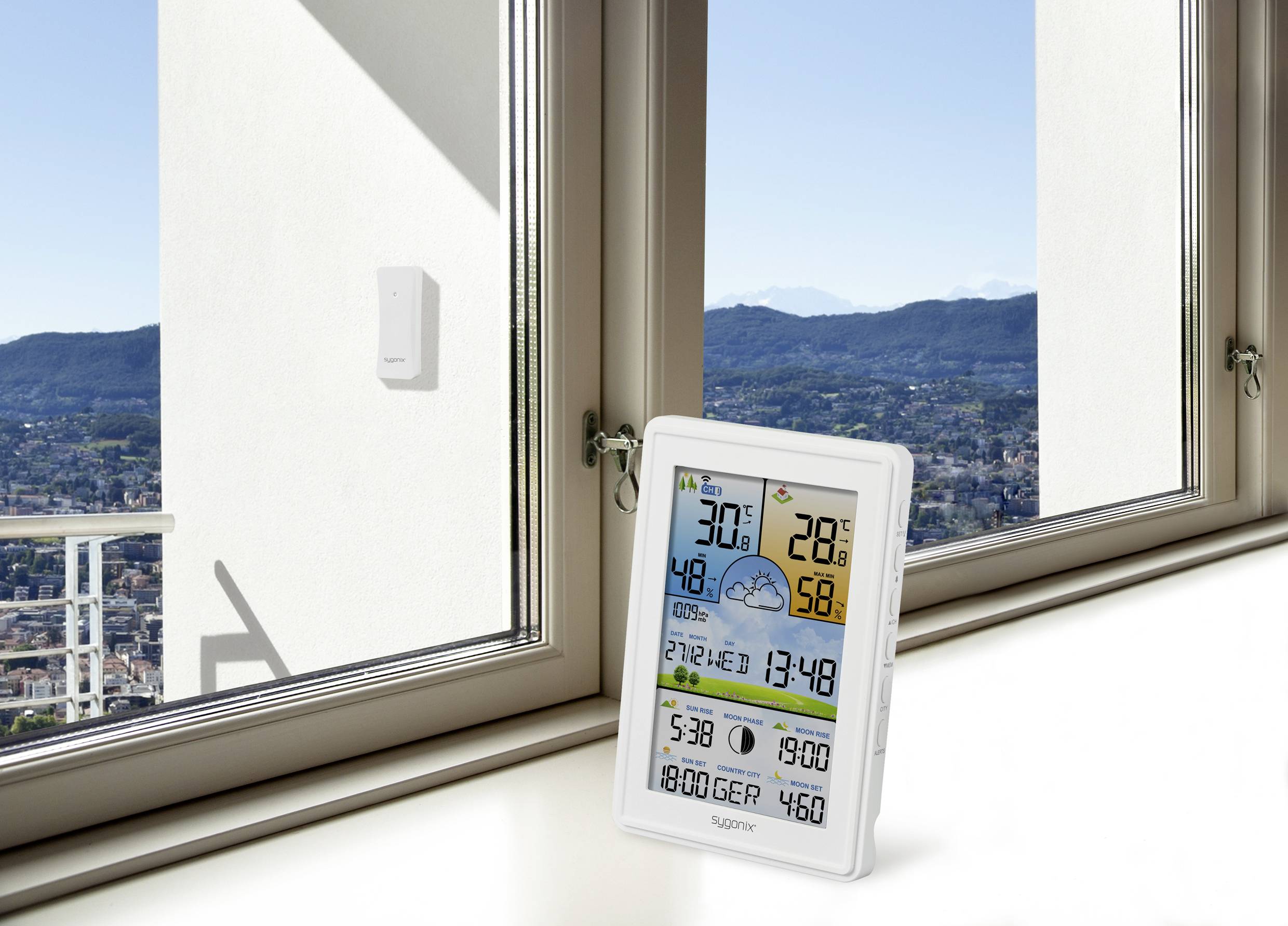 Ein digitales Wetterstationsgerät auf einer Fensterbank zeigt Temperatur, Feuchtigkeit, Uhrzeit und Wettervorhersage an. Hintergrund: Stadtblick.