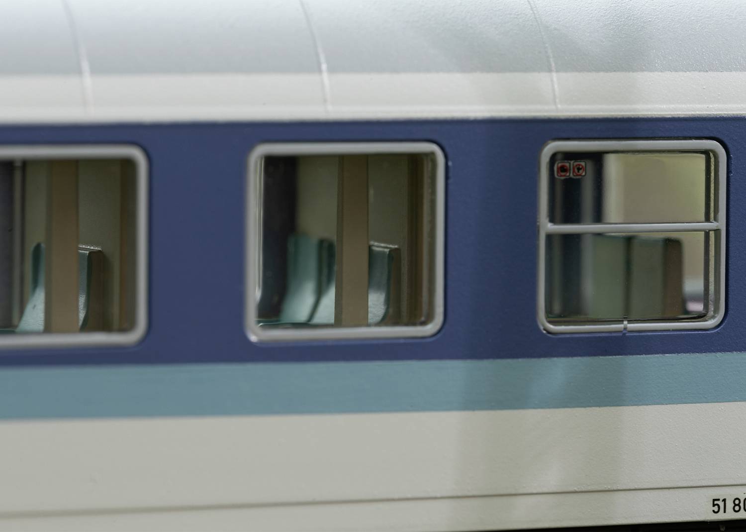 Nahaufnahme eines Modellzugwagens mit blauen und weißen Streifen, sichtbare Fenstersitze und Details der Außenstruktur.
