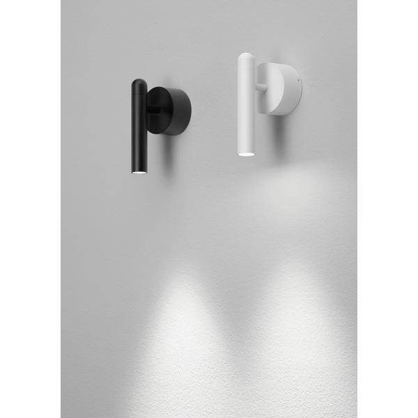 Zwei Wandlampen, links schwarz, rechts weiß, an einer grauen Wand. Beide werfen kegelförmige Lichtstrahlen nach unten.
