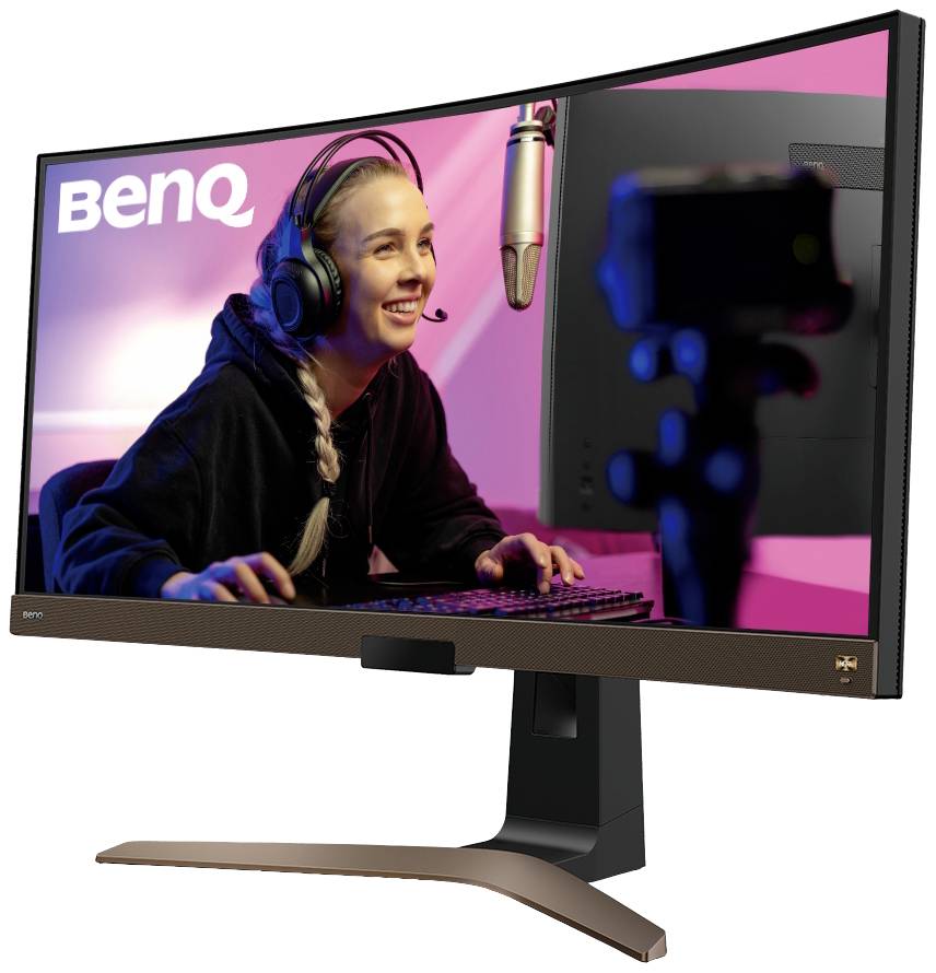 Eine fröhliche Person trägt ein Headset und streamt an einem Computer in einem gut beleuchteten Raum. Im Hintergrund ist ein Mikrofon sichtbar.