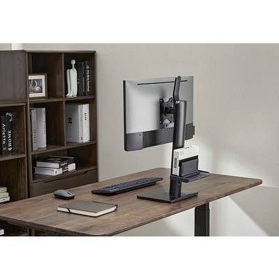 Ein moderner Schreibtisch mit Monitor, Tastatur, Maus und Notizbuch. Im Hintergrund ein Regal mit Büchern und Deko-Objekten.