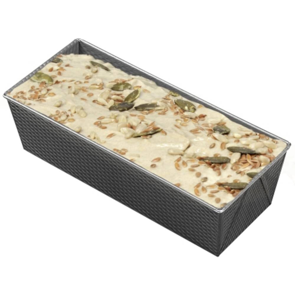 Eine Backform gefüllt mit Teig für ein Brot, das mit Samen wie Kürbiskernen und Leinsamen bestreut ist, bereit zum Backen.