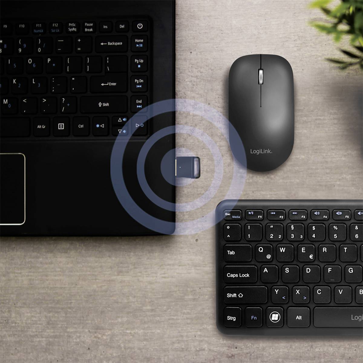 Eine schwarze Tastatur und Maus neben einem Laptop mit einem USB-Empfänger, der in den Laptop gesteckt werden soll. Es gibt eine Zielanzeige um den Empfänger.