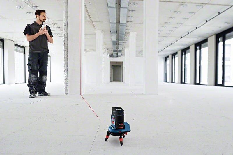 Eine Person in einem leeren Raum verwendet ein Laser-Nivelliergerät zur präzisen Messung von Linien und Punkten.