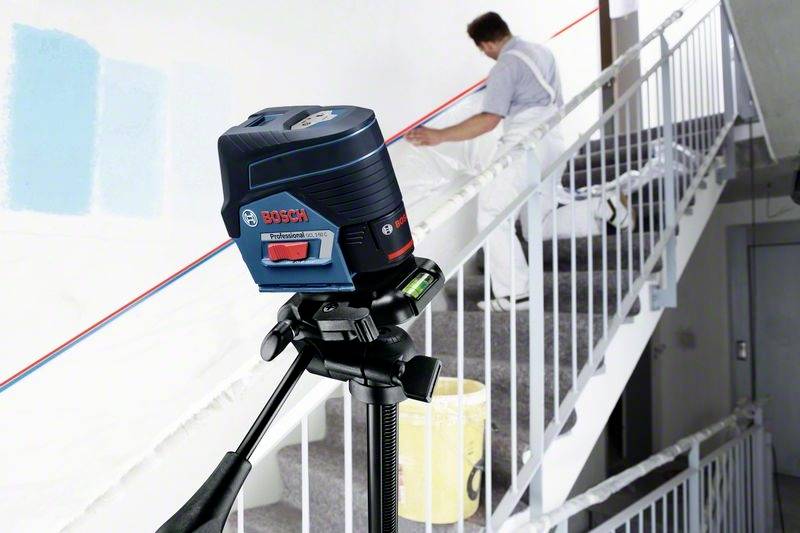 Ein Handwerker streicht eine Treppe weiß. Im Vordergrund steht ein Bosch-Laser-Nivelliergerät auf einem Stativ zur genauen Ausrichtung.