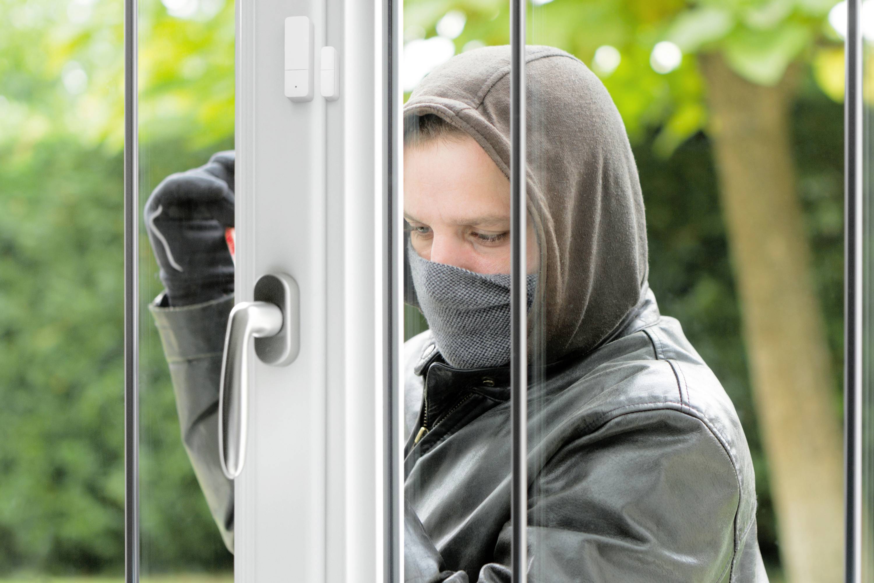 Ein Mann mit Kapuze und Schal versucht, durch eine Tür oder ein Fenster in ein Gebäude einzudringen.