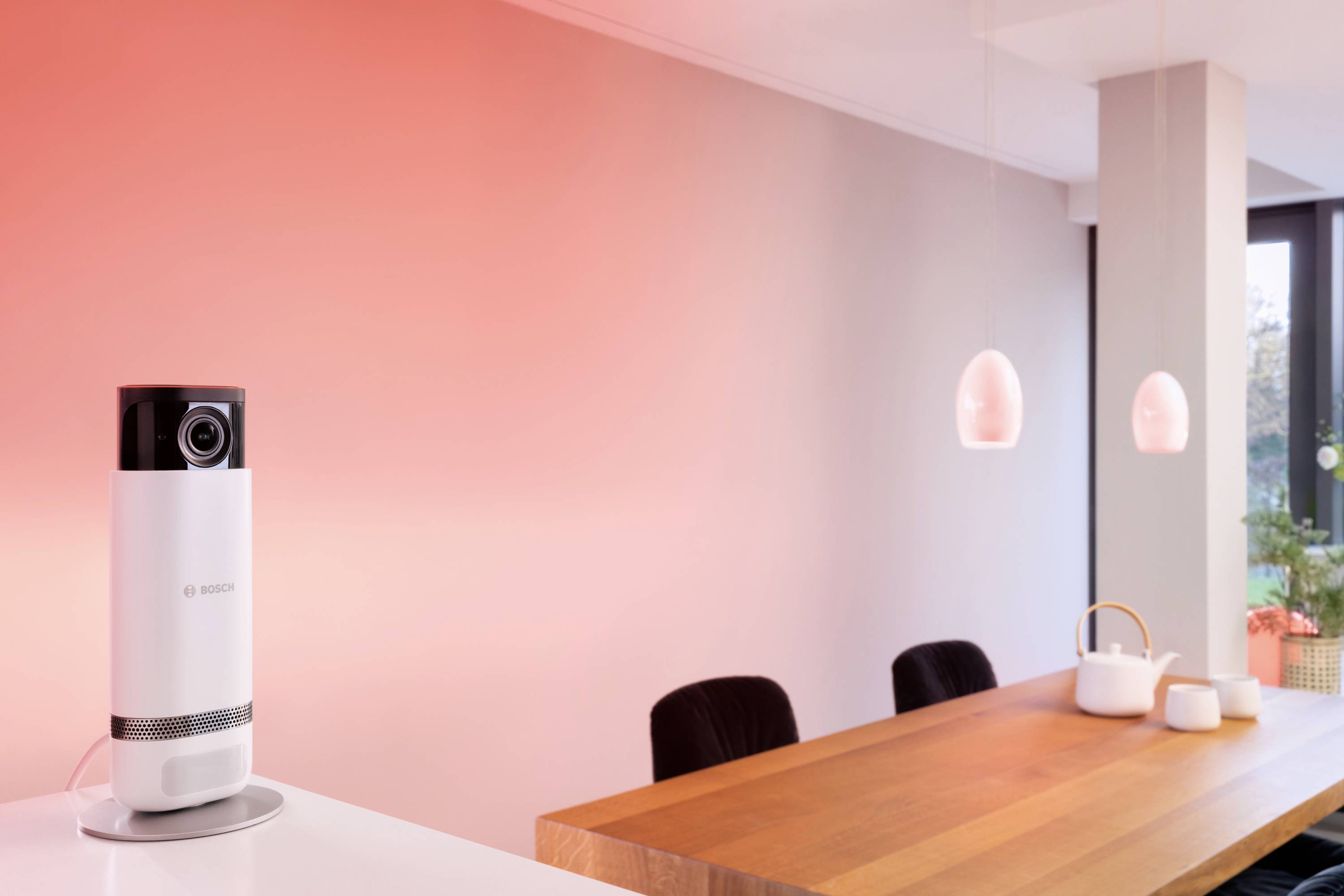 Eine Kamera auf einem Tisch in einem modernen, minimalistisch eingerichteten Raum mit rötlicher Beleuchtung.