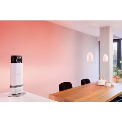 Eine Kamera auf einem Tisch in einem modernen, minimalistisch eingerichteten Raum mit rötlicher Beleuchtung.