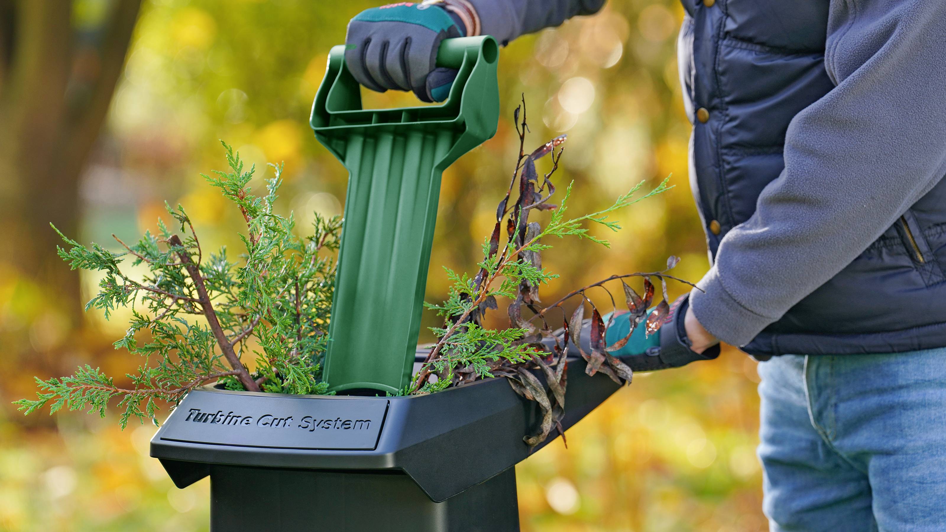 Eine Person verwendet einen Gartenhäcksler, um Zweige und Blätter zu zerkleinern, während sie Gartenhandschuhe trägt.