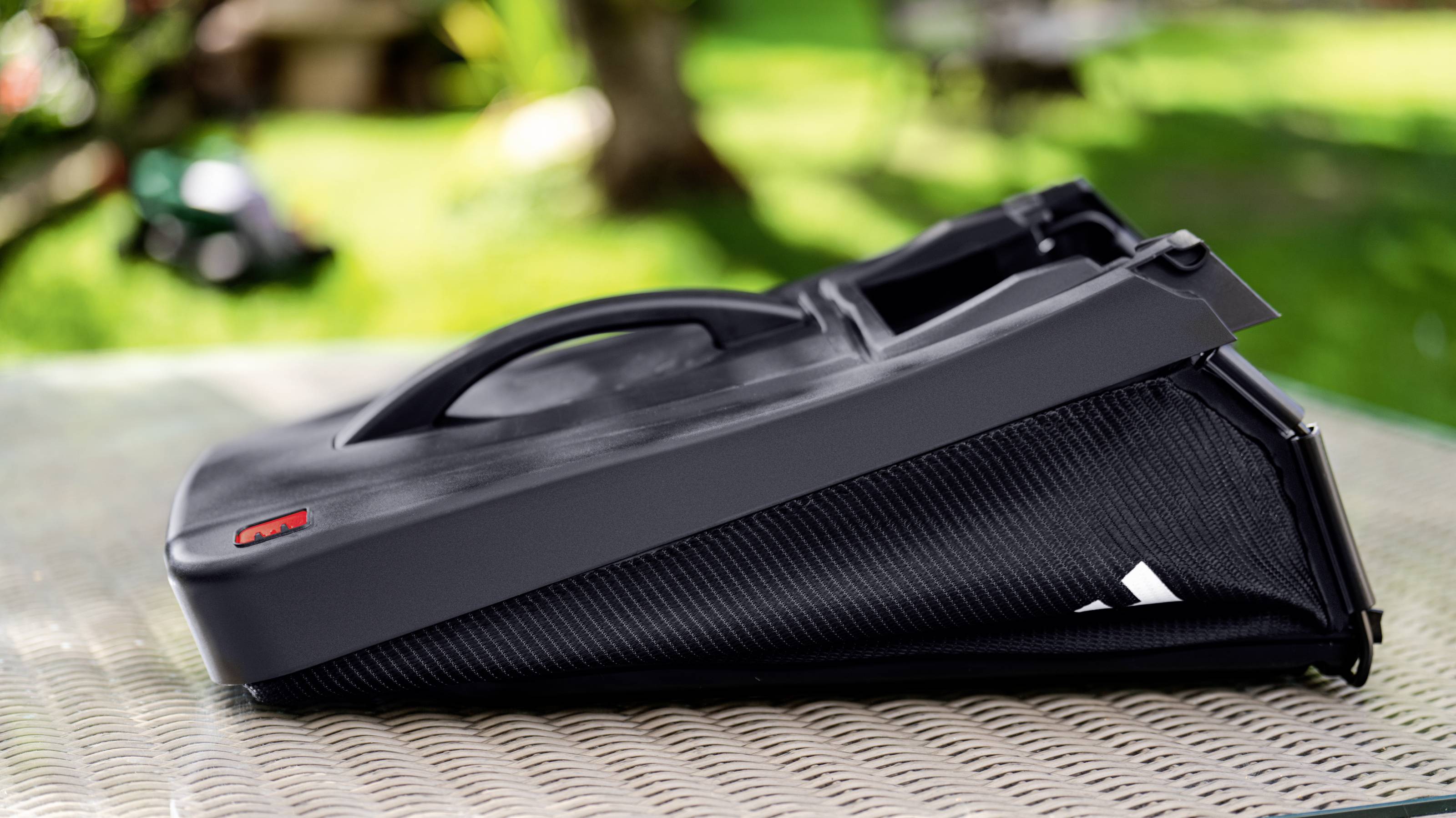 Ein schwarzer, schlanker Fahrradgepäckträger auf einem Tisch im Freien mit unscharfem Hintergrund eines Gartens, ideal für den Transport.
