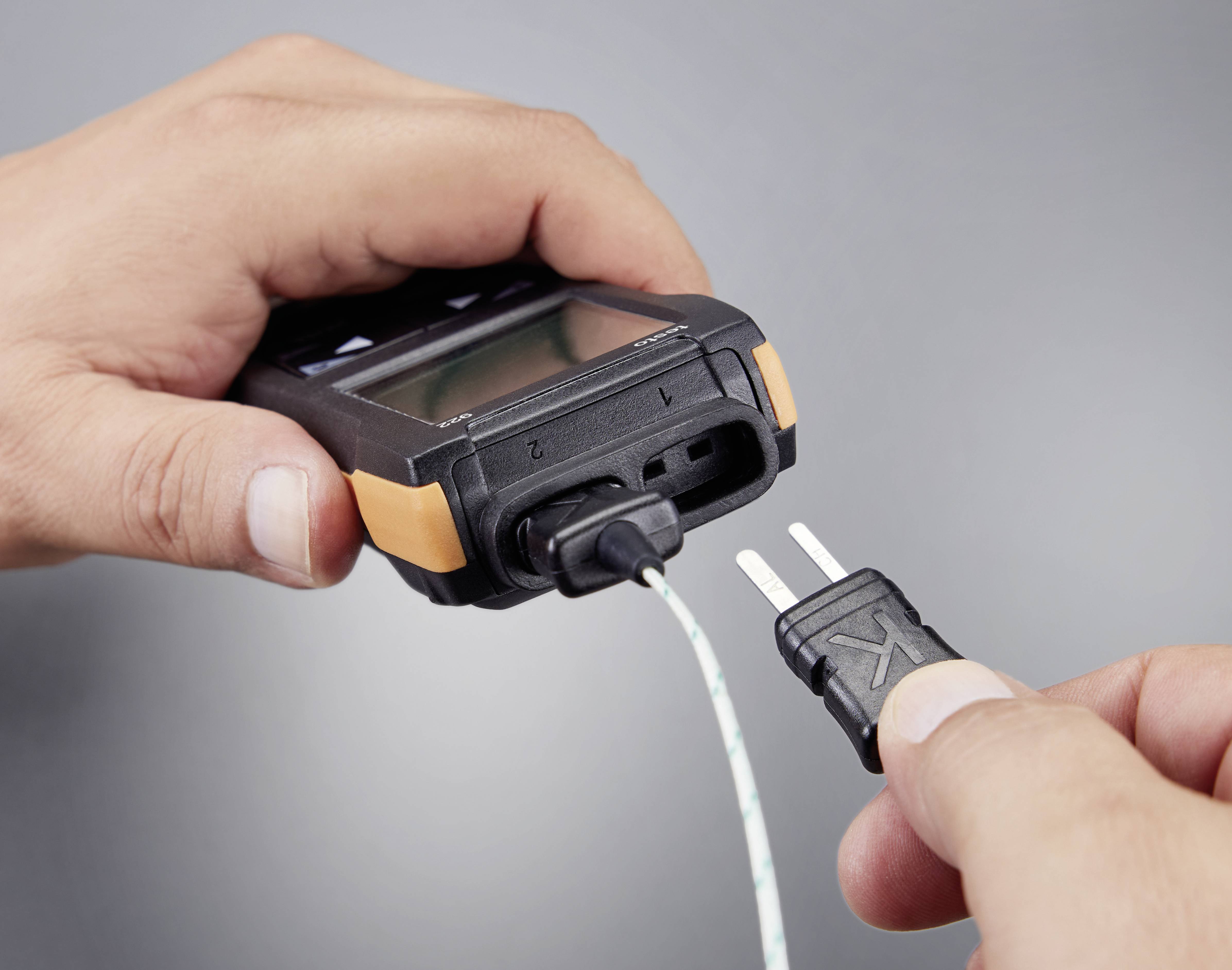 Eine Person steckt ein K-Thermoelement in ein Temperaturmessgerät ein, um eine Messung durchzuführen.