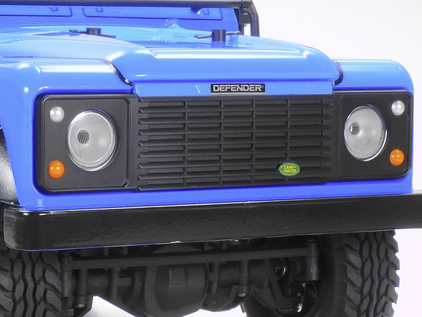 Ein blaues Modell eines Geländewagens mit markanter Front und runden Scheinwerfern. Markenzeichen 'Land Rover Defender' sichtbar.