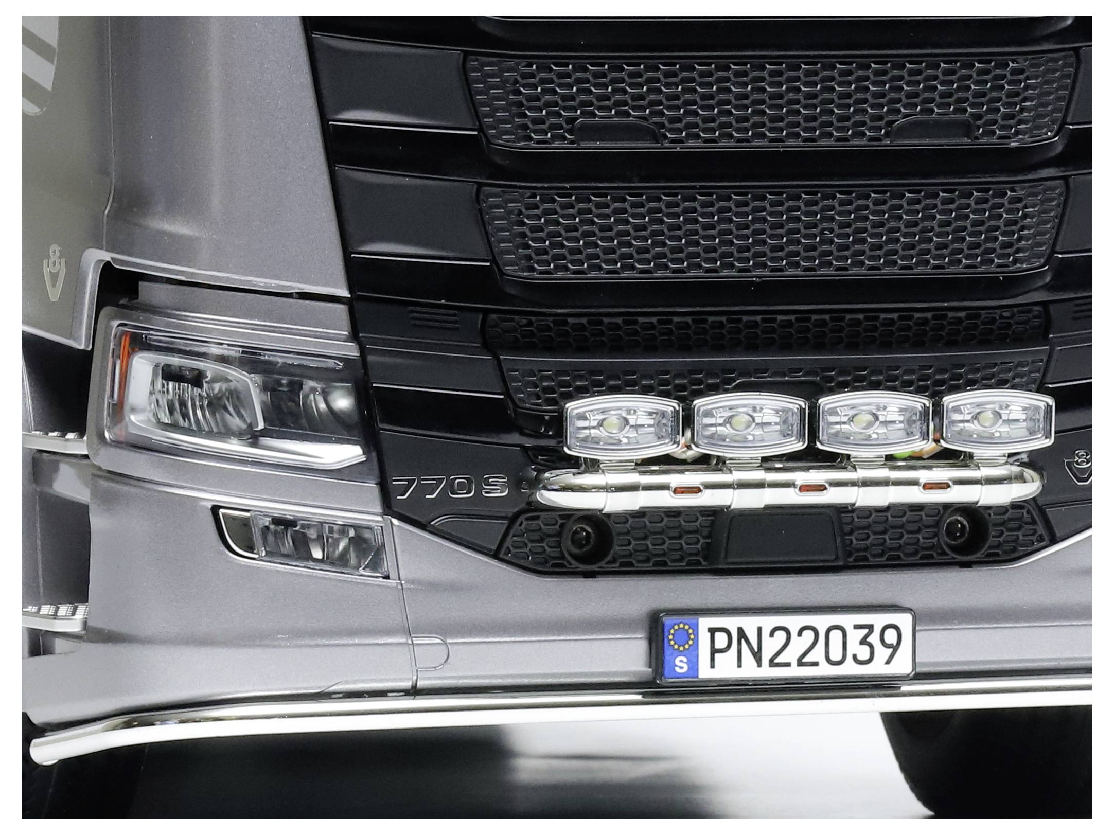 Ein grauer Lkw mit Scheinwerfern und einem Nummernschild 'PN22039' an der Front. Hauptscheinwerfer auf schwarzem Kühlergrill.