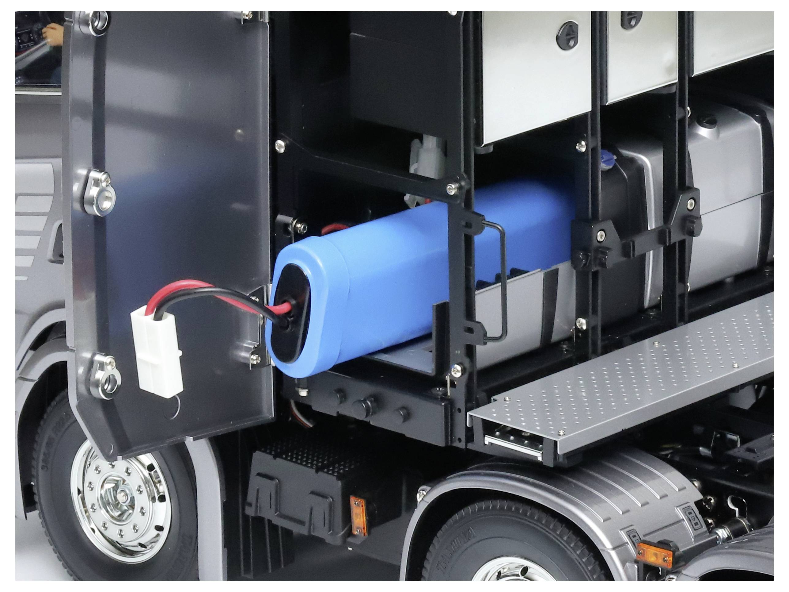 Ein blauer zylindrischer Akku ist an der Buchse eines Modell-LKWs angeschlossen. Der LKW ist teilweise geöffnet, um den Akku zu zeigen.