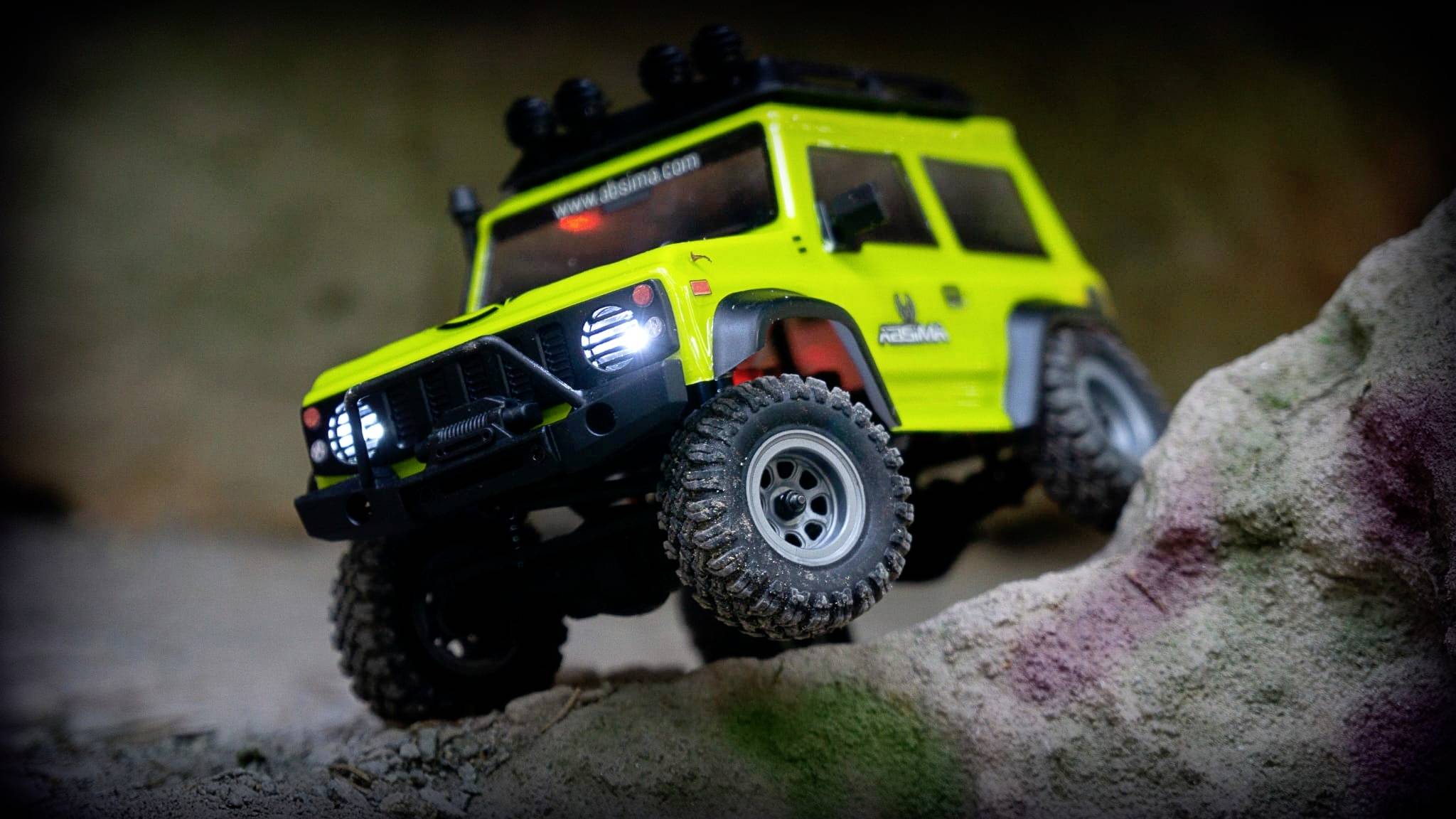 Ein leuchtend grünes, ferngesteuertes Auto im Offroad-Stil klettert über einen Felsen, die Scheinwerfer leuchten.