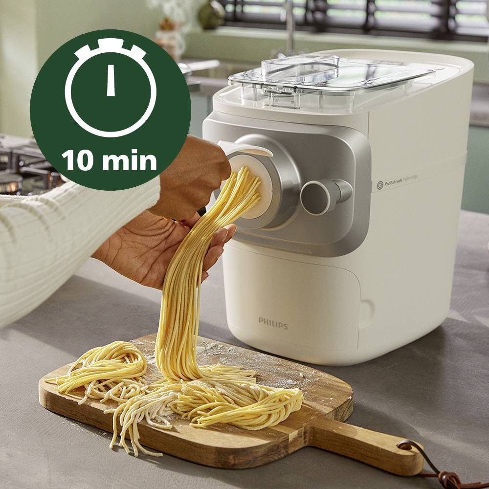 'Pastamaker extrudiert frische Pasta, bereit zum Kochen. Eine Stoppuhr zeigt 10 Minuten Kochzeit an. Küchengerät auf Küchenarbeitsplatte.'