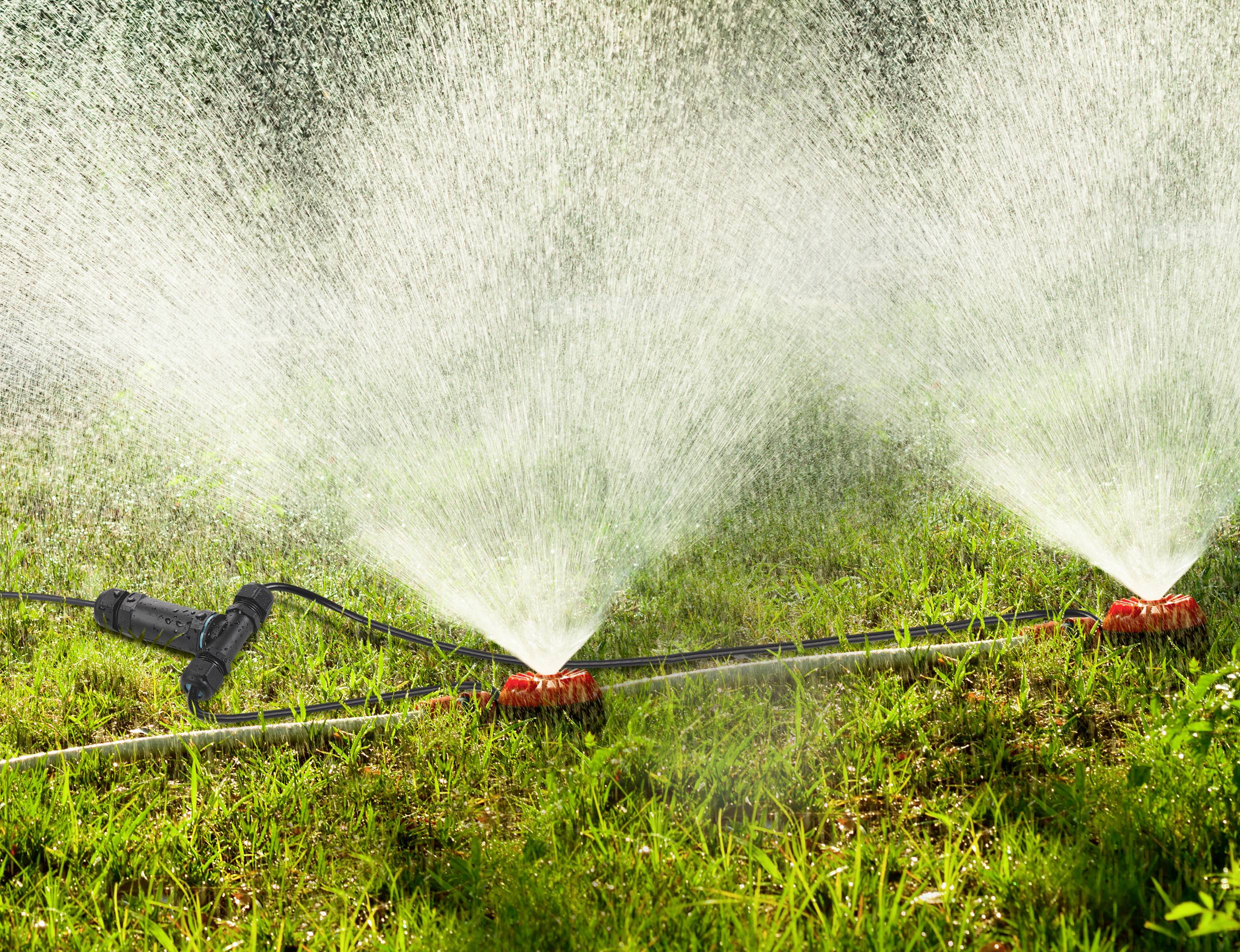 'Ein Rasensprenger bewässert grünen Rasen bei Tageslicht, verteilt gleichmäßig Wasserstrahlen.'