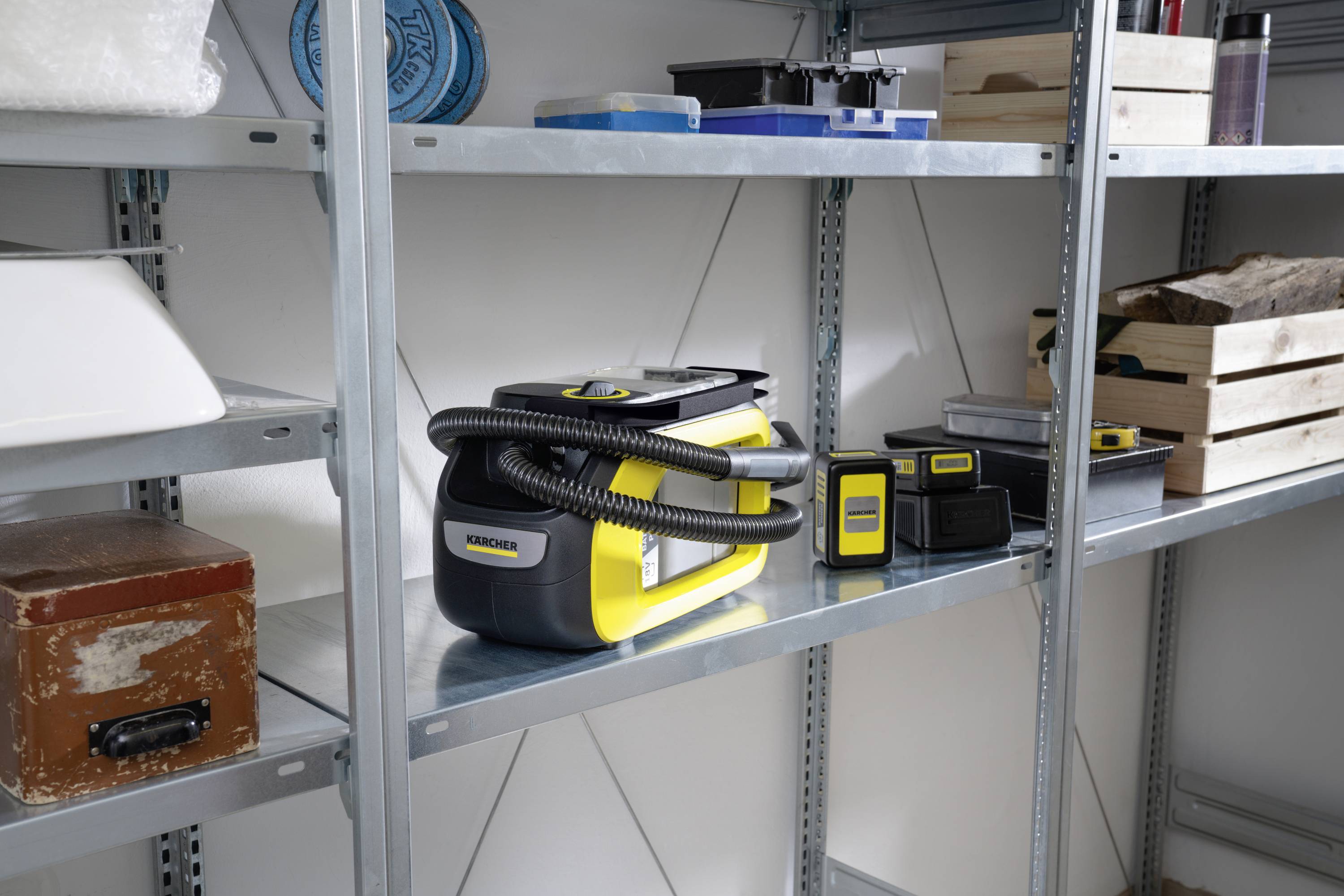 Gelbe und schwarze Reinigungsgeräte auf einem Metallregal in einem Lagerraum. Daneben liegen weitere Haushaltsgegenstände und Boxen.
