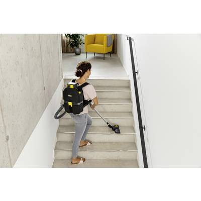 Person reinigt Treppe mit einem Rucksackstaubsauger. Im Hintergrund steht ein gelber Sessel.