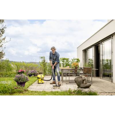 Ein Mann reinigt mit einem gelben Nass-Trockensauger eine Terrasse. Im Hintergrund sind Pflanzen und Gartenmöbel sichtbar.