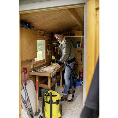 Ein Mann arbeitet in einer Holzwerkstatt. Er steht an einem Tisch und bearbeitet ein Holzstück mit einer Säge. Um ihn liegen Werkzeuge und Geräte.