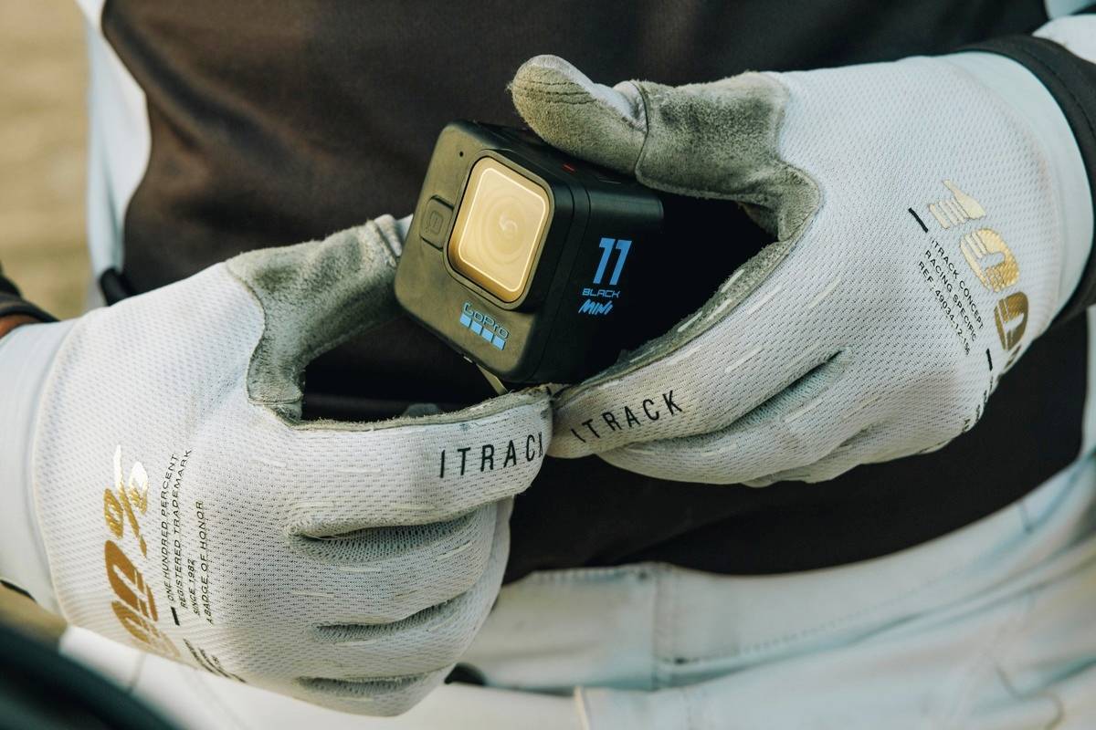 Eine Person hält eine GoPro-Kamera mit beiden Händen, bekleidet mit grauen Handschuhen. Hauptfokus: die Kamera.