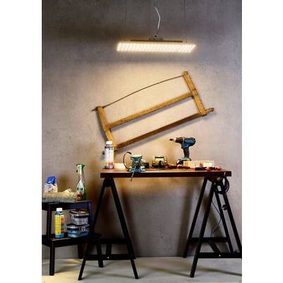 Arbeitsbereich mit Tisch; darauf liegen Werkzeug und Materialien wie Bohrmaschine und Schraubenschlüssel. An der Wand hängt ein alter Holzrahmen.