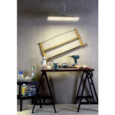 Eine Werkbank mit Werkzeugen und Materialien, darunter Bohrmaschine, Klebeband, Spraydosen und eine Lampe über einem hölzernen Rahmen an der Wand.